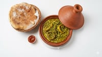 • طاجين بازلاء وأرضي شوكي مغربي تقليدي مع سلة خبز وصلصة حمراء على خلفية بيضاء.
