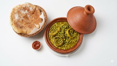 • طاجين بازلاء وأرضي شوكي مغربي تقليدي مع سلة خبز وصلصة حمراء على خلفية بيضاء.